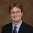 Headshot of a smiling man wearing glasses and a suit with a tie.